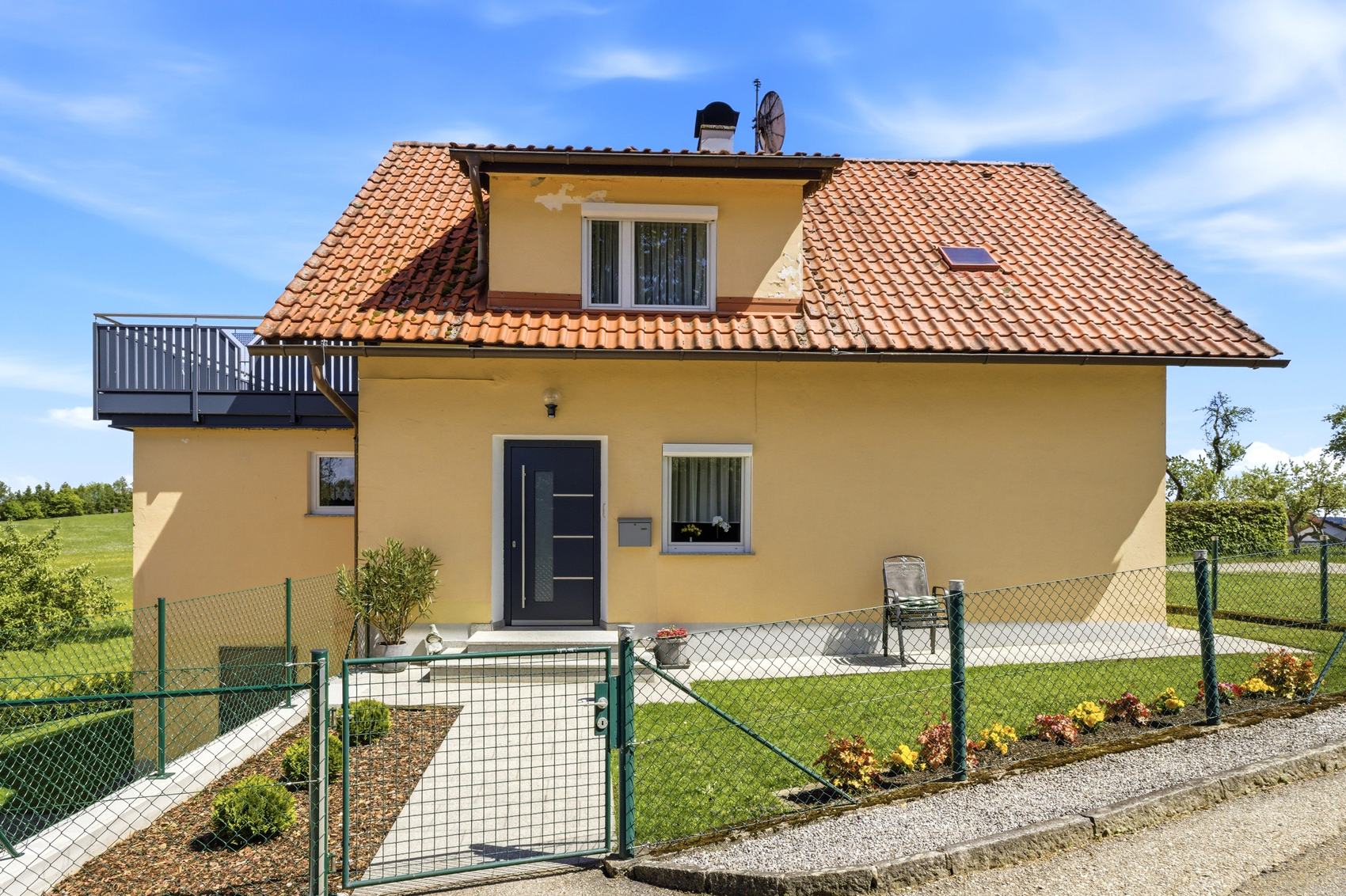 Gelbes Einfamilienhaus mit rotem Dach und Zaun