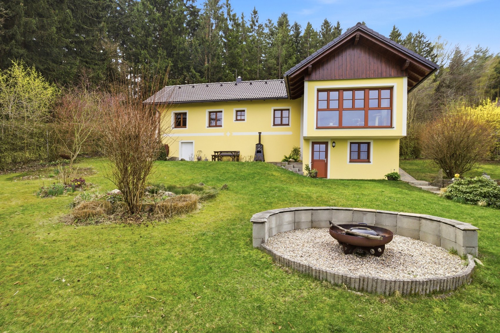 Gelbes Einfamilienhaus mit Garten und Feuerstelle unter blauem Himmel