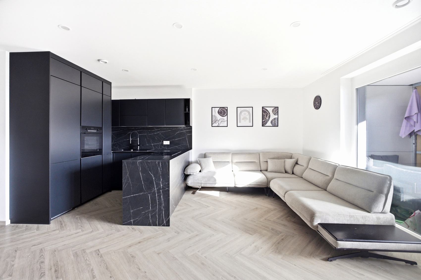 Wohnzimmer mit heller Couch und dunkler Küche