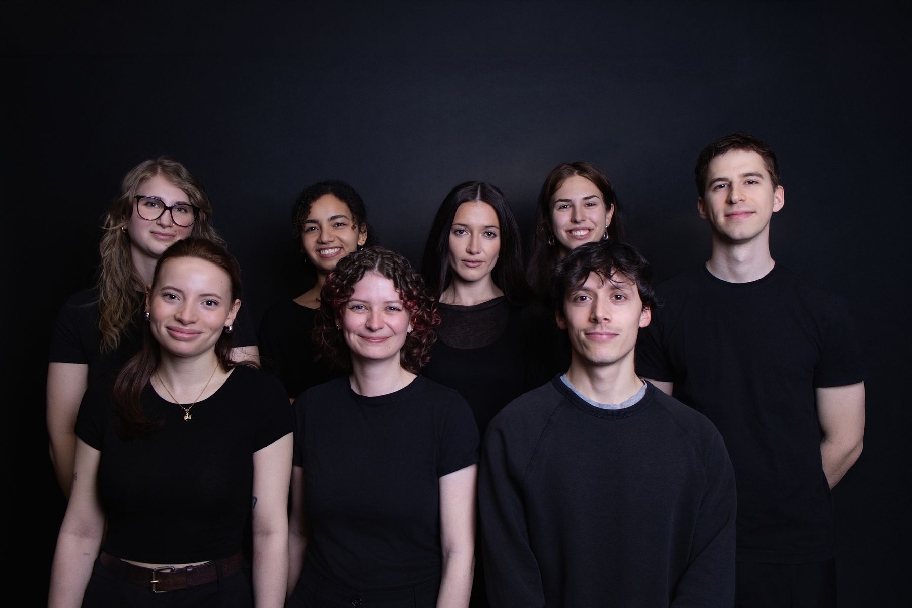 Gruppenbild eines Teams in Schwarz vor dunklem Hintergrund